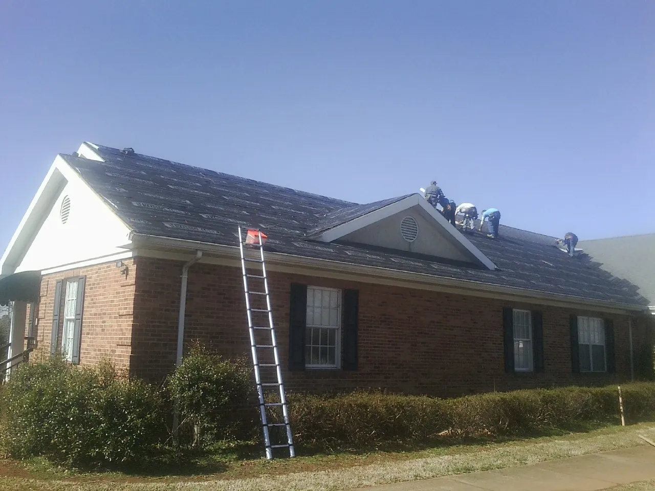 Crew tearing shingles off a brick ranch roof with a ladder set — Emergency Roof Repair work by our crew in Baldwin