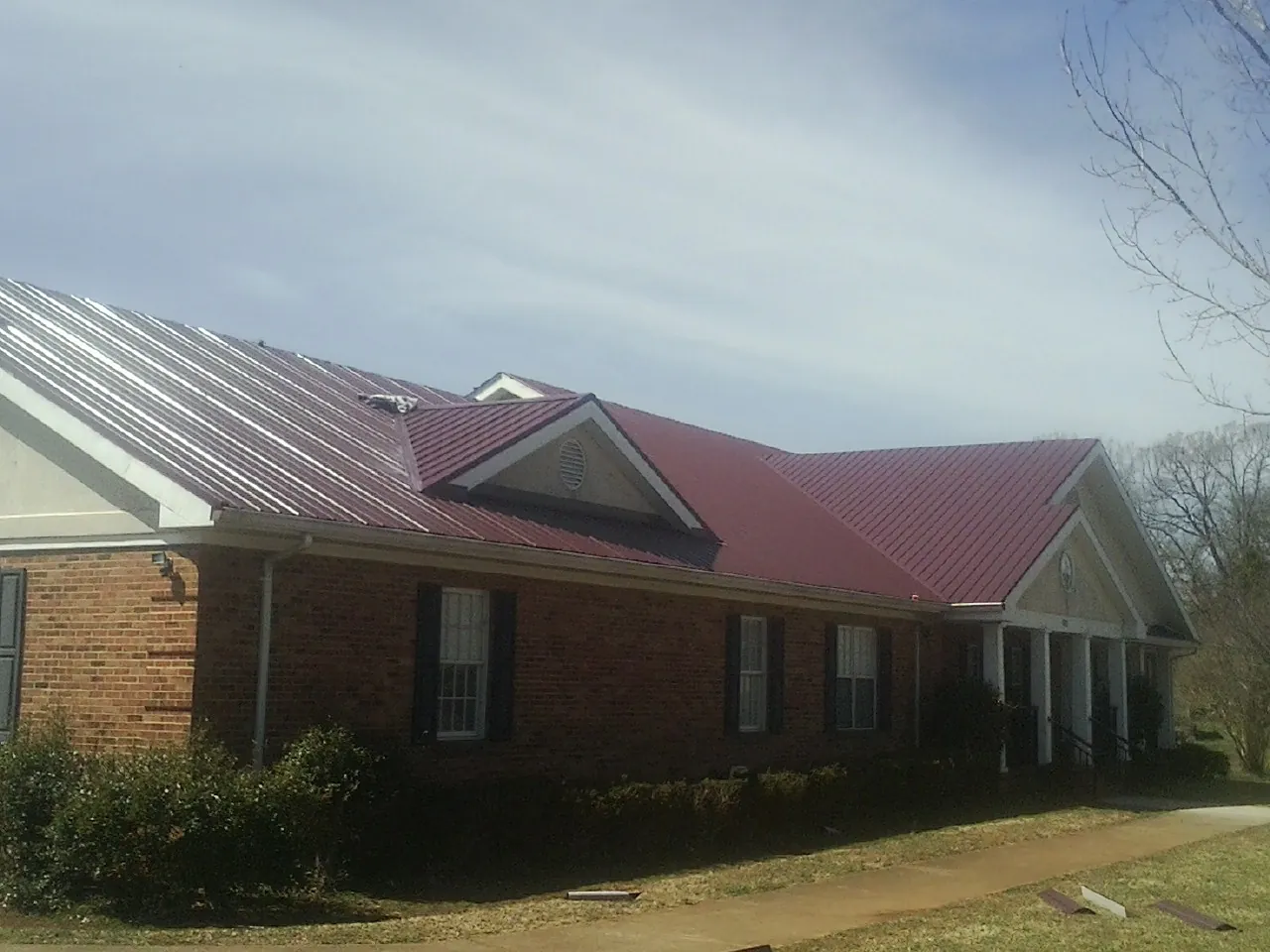 Red metal roof with gabled entries on a long brick building, from a Hail Damage Roof Repair job in Baldwin